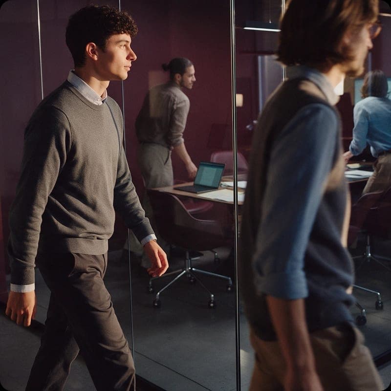 A colleague walking through a modern office past a glass-walled meeting space.