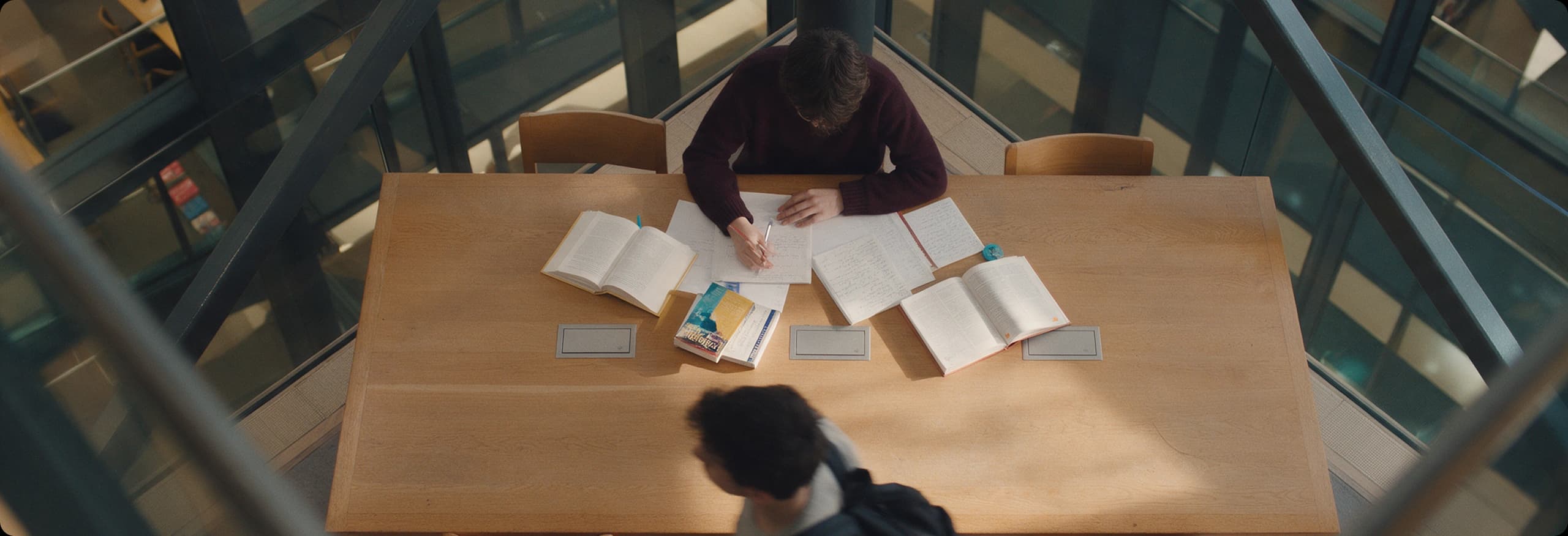 A student writing at a table spread with open books